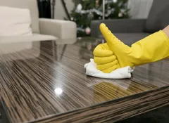 Úklid dřevěného stolu v obýváku, ruka v gumové rukavici utírá povrch hadrem.