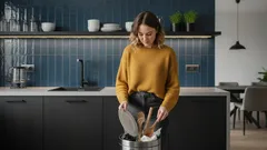 Žena v moderní kuchyni vyhazuje odpadky do koše, ekologické třídění odpadu doma.