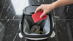Vyhazování houbičky do odpadkového koše na černé dlažbě v kuchyni
